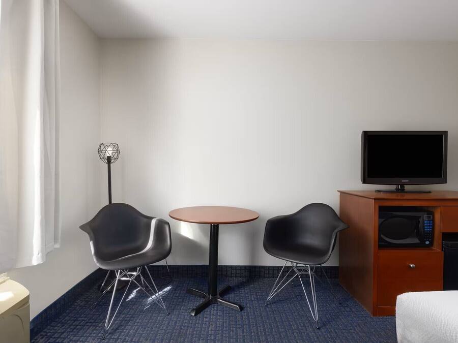 A hotel room with a bed, a desk with a television, two chairs, a small table, and a floor lamp.