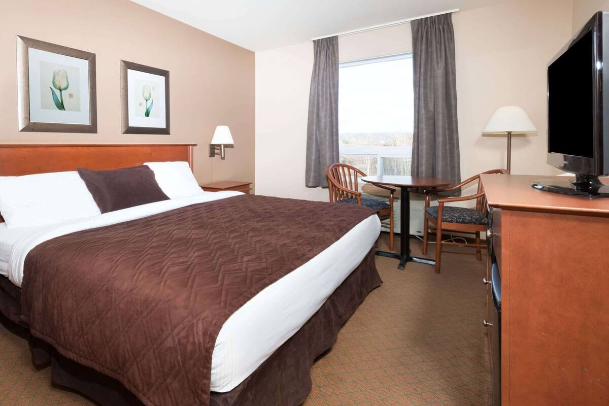 Ein Hotelzimmer mit einem großen Bett, einem Schreibtisch mit Stuhl, einem Fernseher und zwei gerahmten Bildern an der Wand.