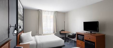 Habitación de hotel con dos camas, un escritorio, televisión, una silla y una mesita.