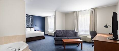 Habitación de hotel con cama, sofá, escritorio, televisor, baño con bañera y ventana con cortinas.