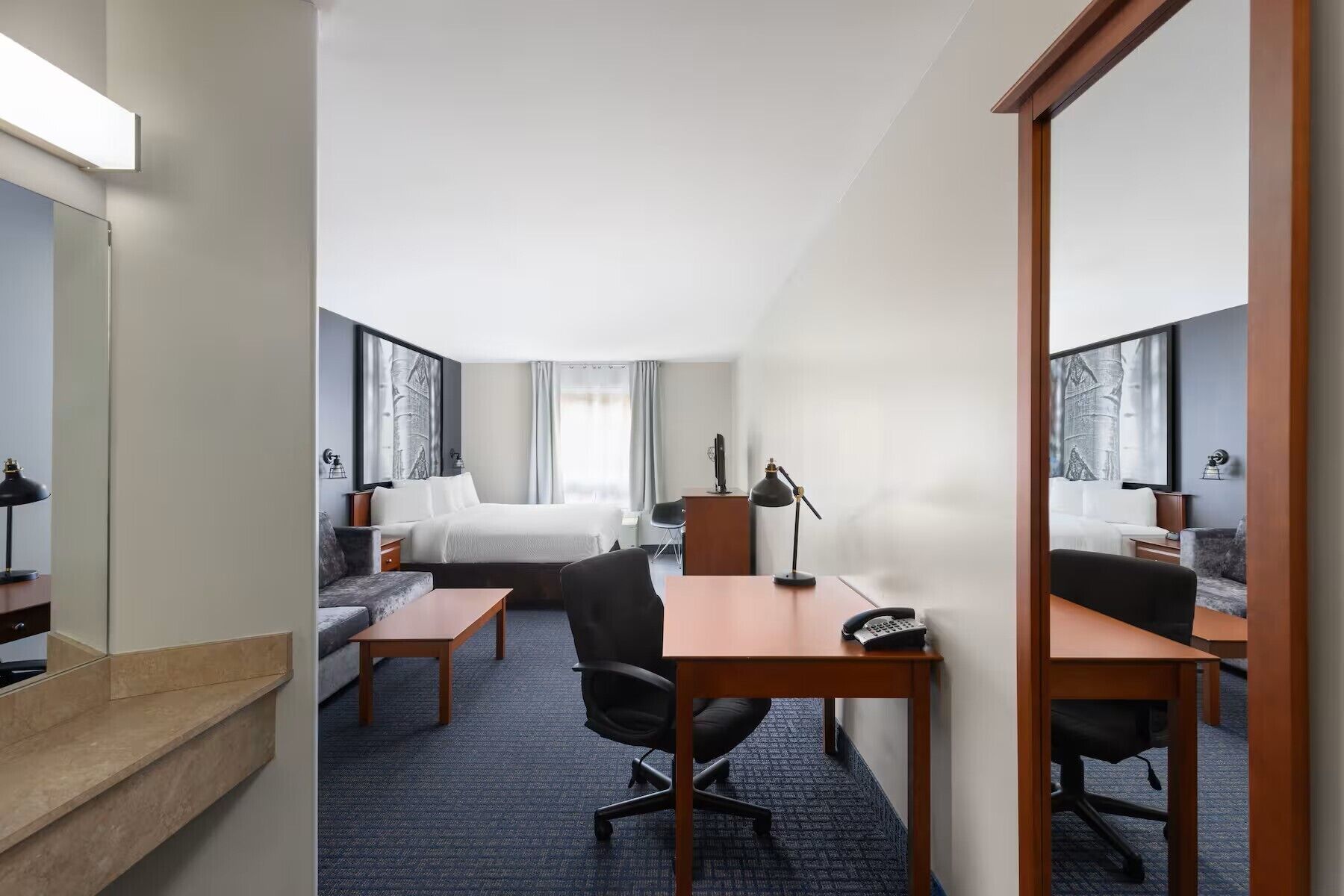 Quarto de hotel com cama, escrivaninha, cadeira e um espelho grande.