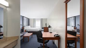 Quarto de hotel com cama, escrivaninha, cadeira e um espelho grande.