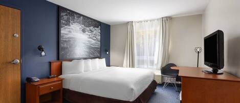 A hotel room with a bed, bedside table, desk, chair, television, and a large window with curtains.