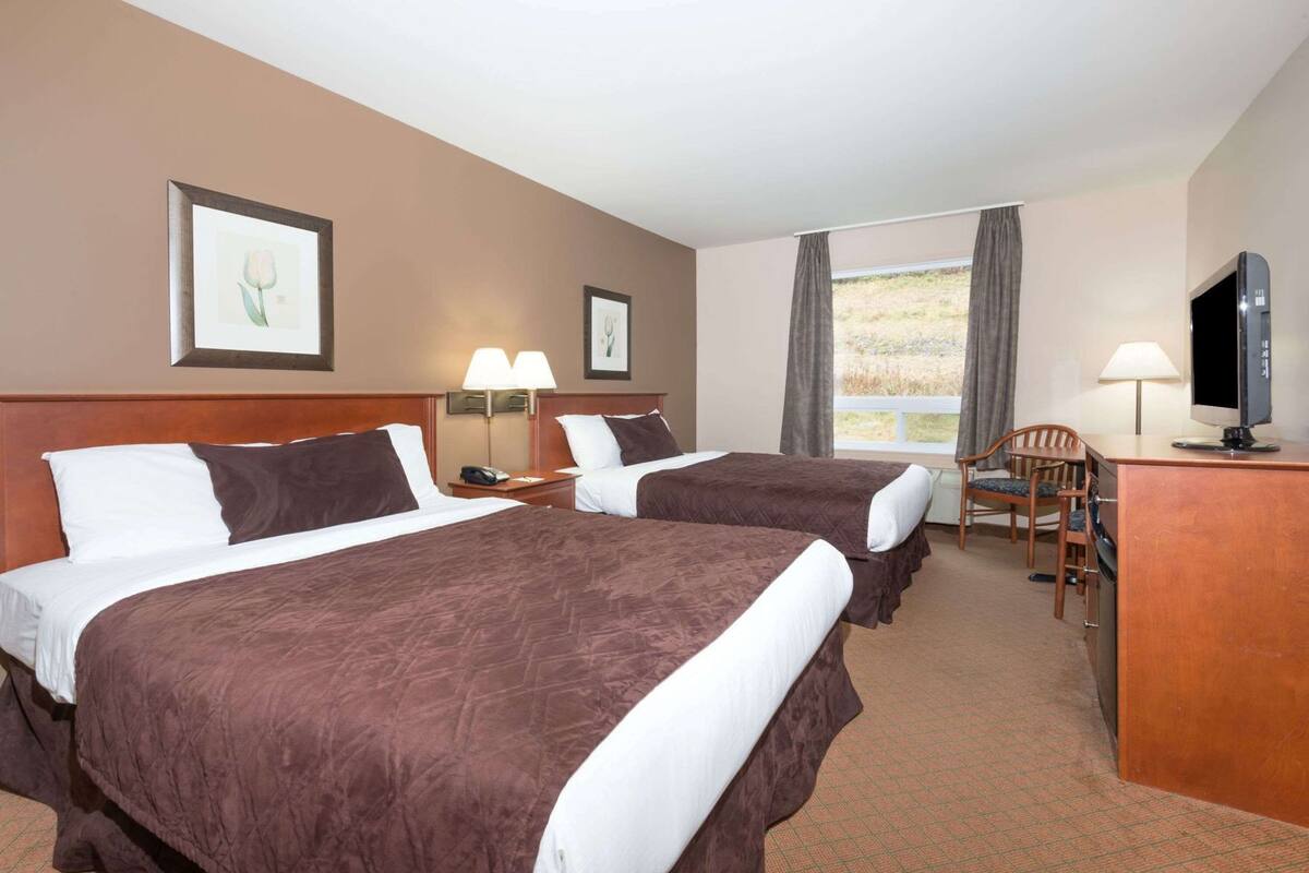 Ein Hotelzimmer mit zwei Betten, einem Schreibtisch mit Fernseher, einem Sessel und einem Fenster mit Blick.