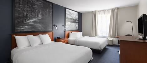 A hotel room with two beds, a desk, a TV, and artwork on the walls.