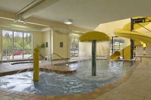 An indoor swimming pool with a water slide, a hot tub, and a sun terrace with outdoor seating. - Terra Laurentides (Sainte-Agathe-des-Monts)