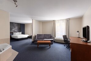 A hotel room with a bed, a sofa, a desk with a computer, a TV, a window with curtains, and a bathroom with a bathtub. - Hôtel TERRA Laurentides (Sainte-Agathe-des-Monts)