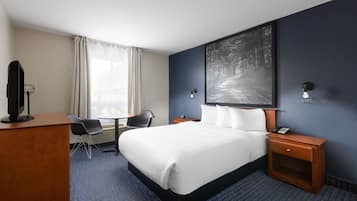 A hotel room with a bed, a desk with a computer, a chair, a nightstand with a phone, and a large window with curtains.