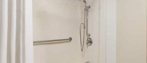 Un espace douche équipé d’un pommeau de douche à main, d’un flexible de douche et d’une barre d’appui.