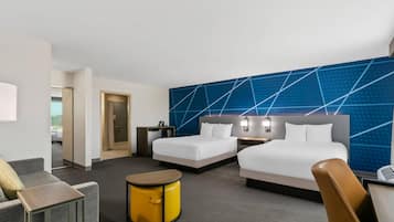 Habitación de hotel con dos camas, un escritorio, una silla, una mesita y una pared con diseño geométrico.