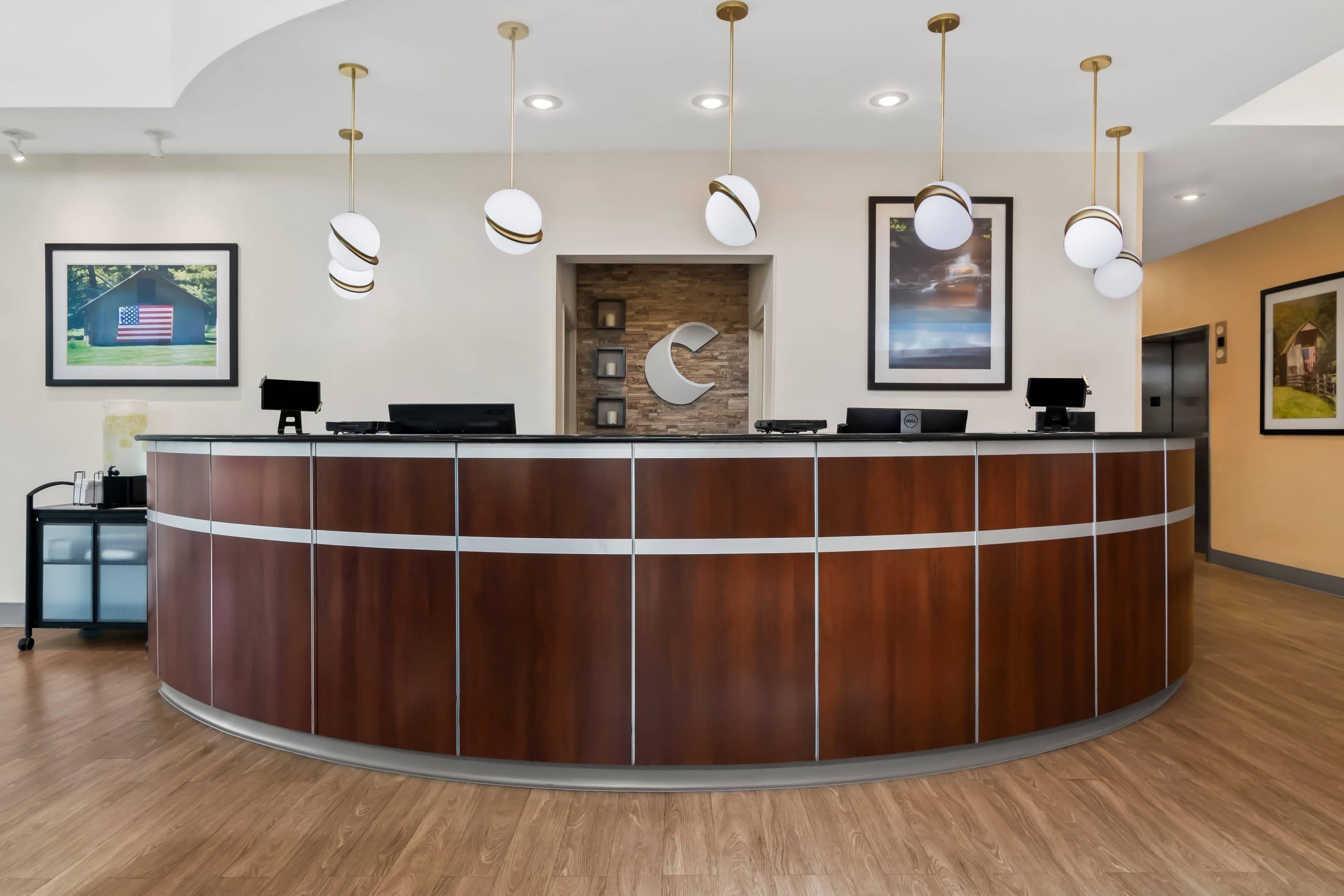 A reception desk with a wooden finish, multiple light fixtures, framed artwork on the walls, and a small cart with a computer.