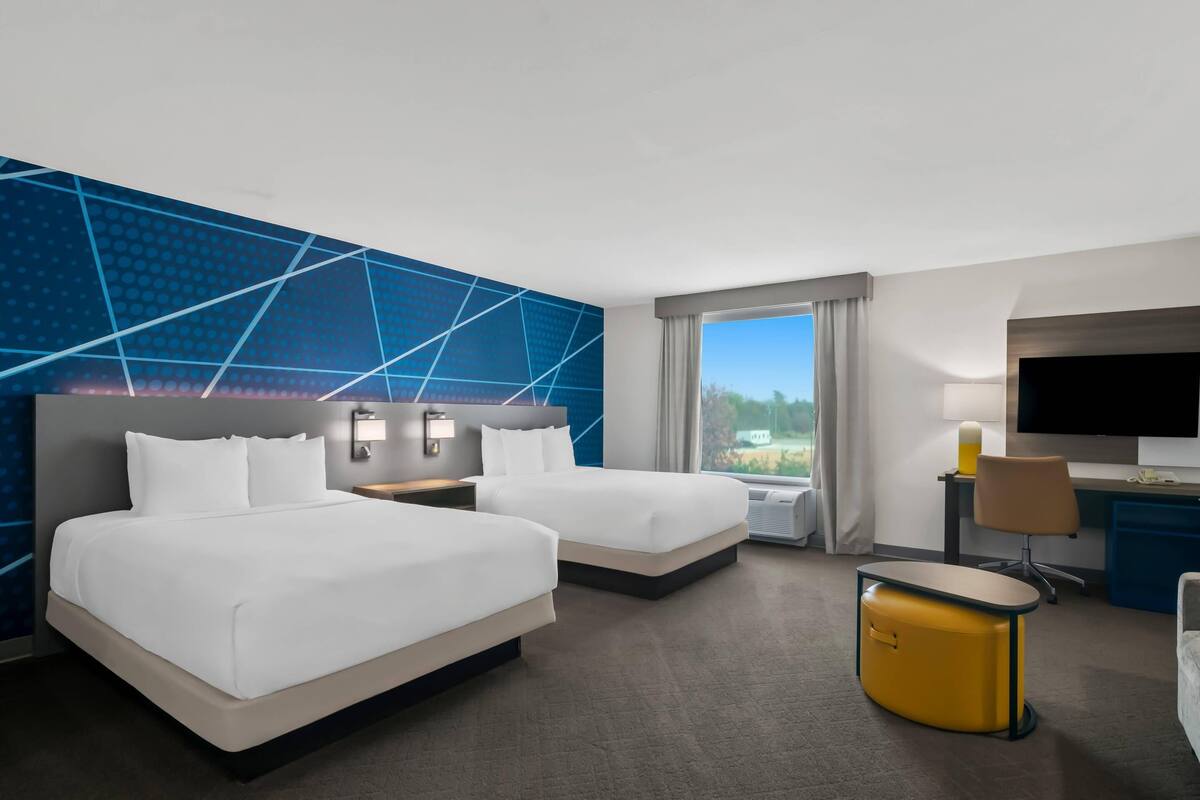 Habitación de hotel con dos camas, un escritorio, un televisor y vistas al exterior.