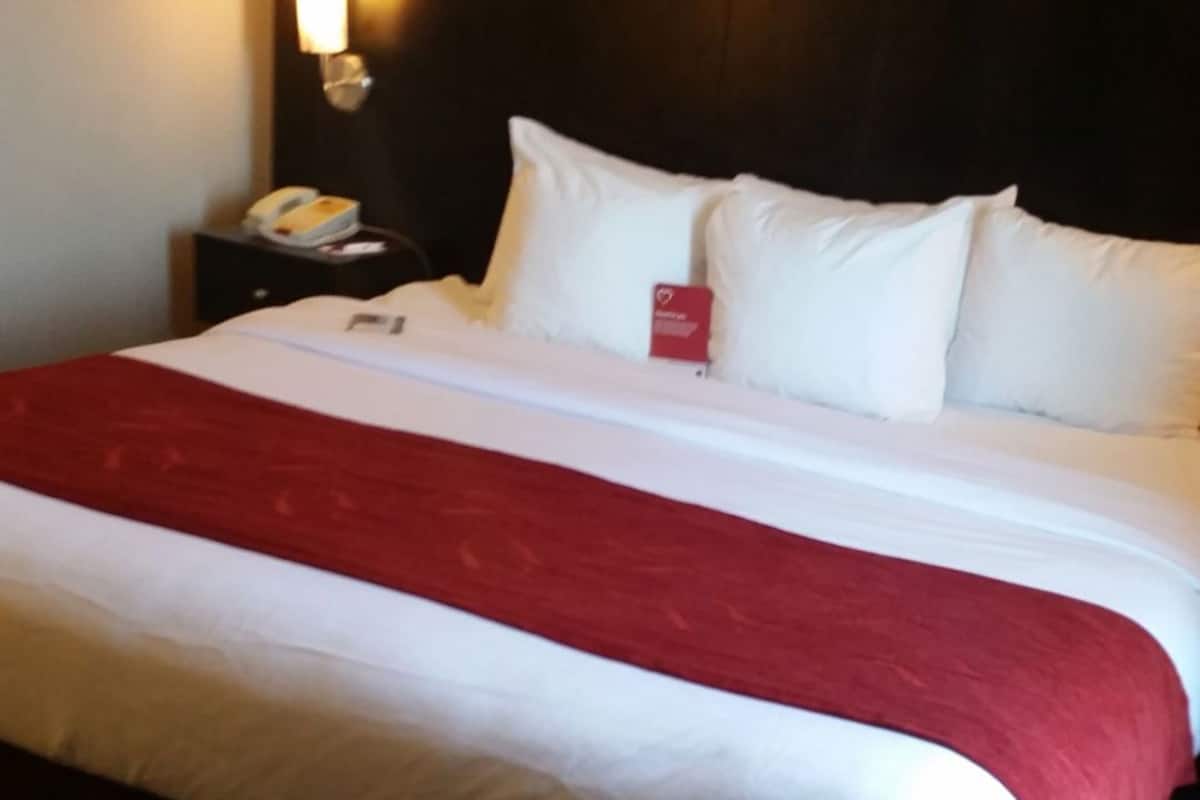 Habitación de hotel con una cama grande, cabecero, mesita de noche con lámpara y teléfono.