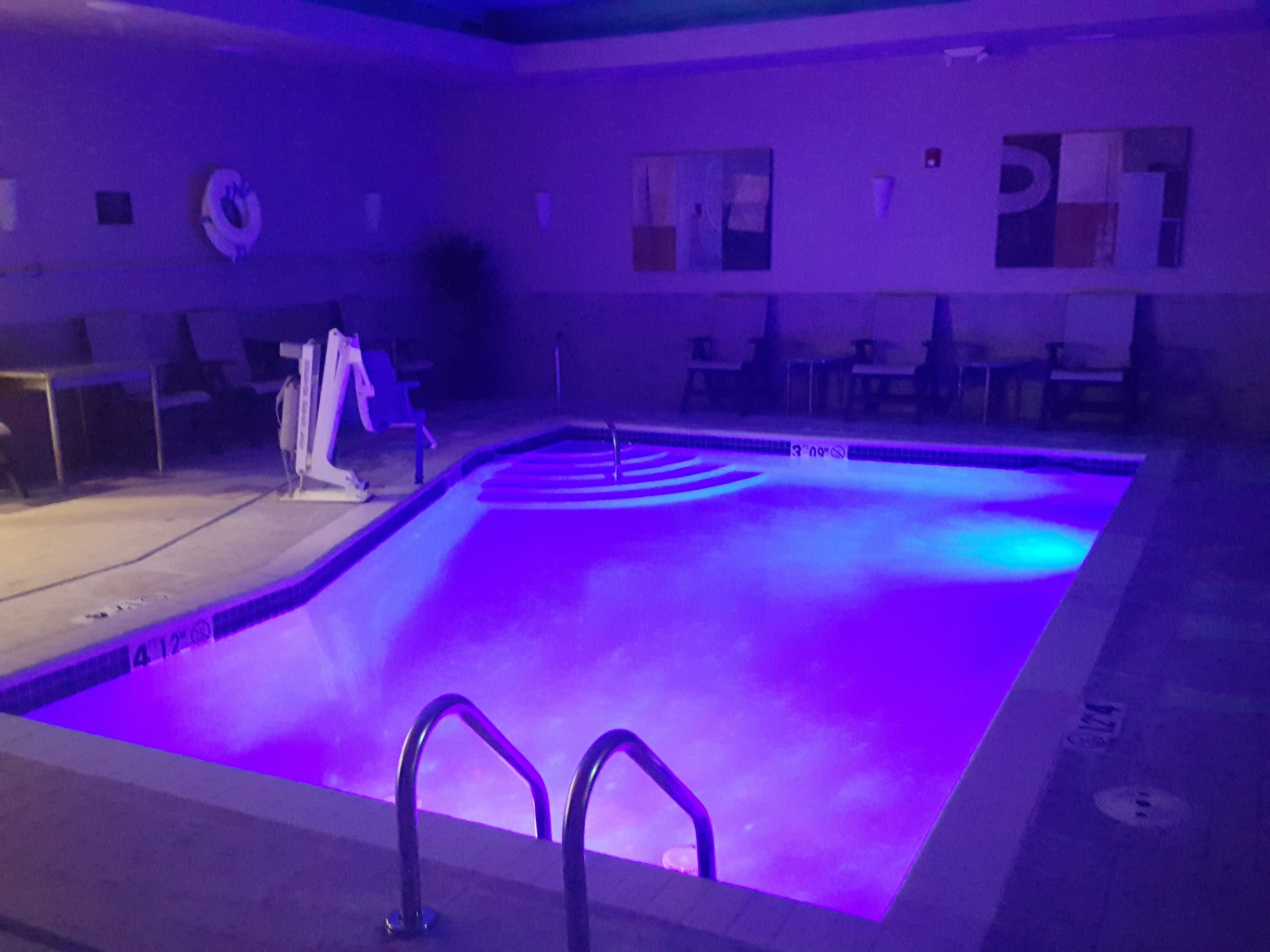 Une piscine éclairée de lumière violette, une bouée de sauvetage et une chaise.