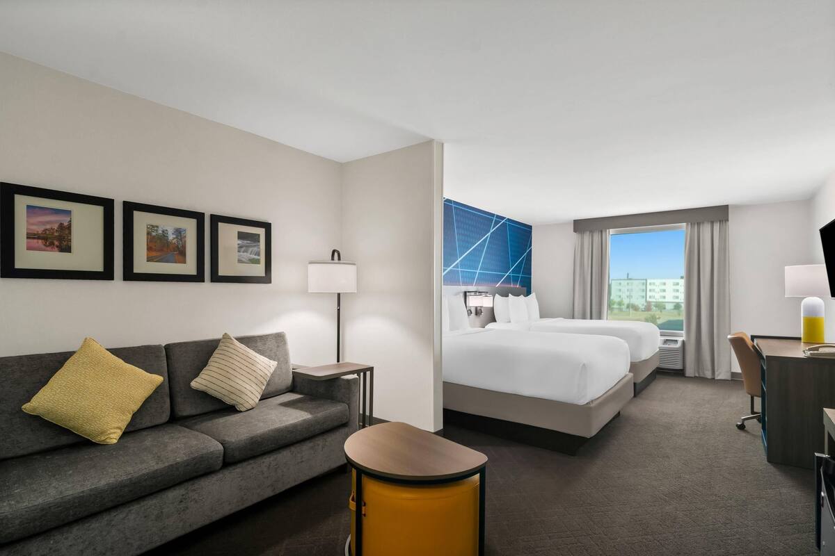 Habitación de hotel con sofá, dos camas, escritorio, silla y cuadros en la pared.