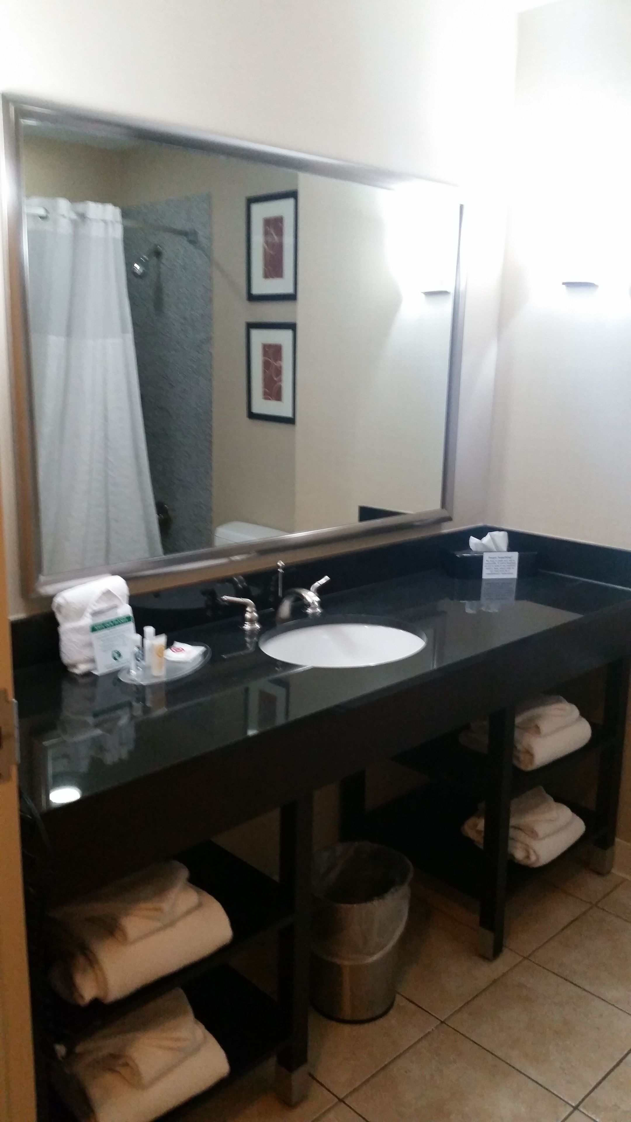 Une salle de bain avec un grand miroir, un lavabo blanc, un porte-serviettes et une poubelle.