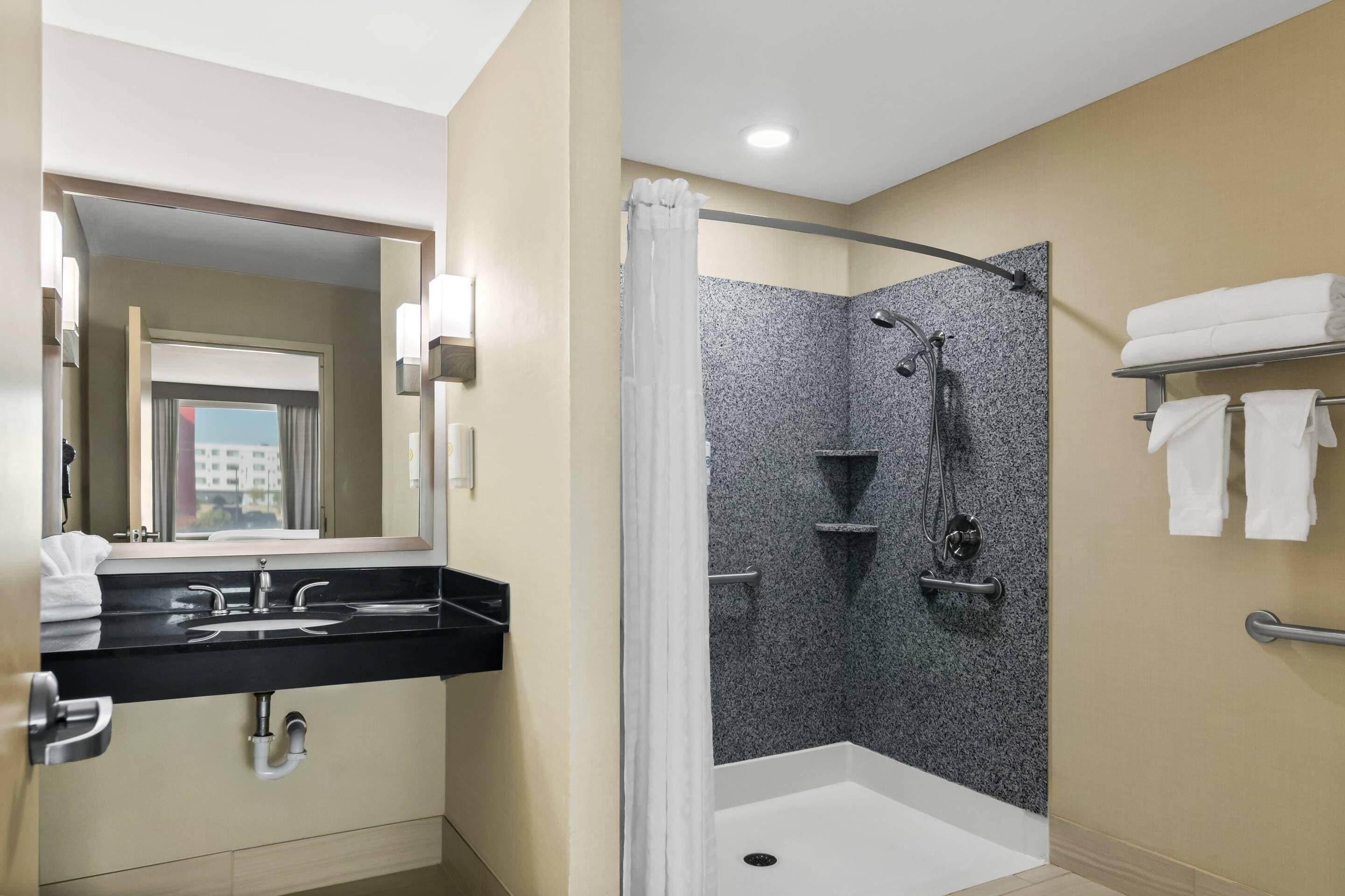 A modern bathroom with a black sink, a shower with a glass door, and a mirror with lights.
