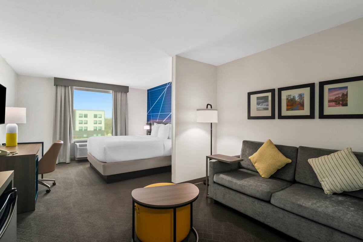 Habitación de hotel con cama, sofá, escritorio, silla, lámpara y cuadros en la pared.