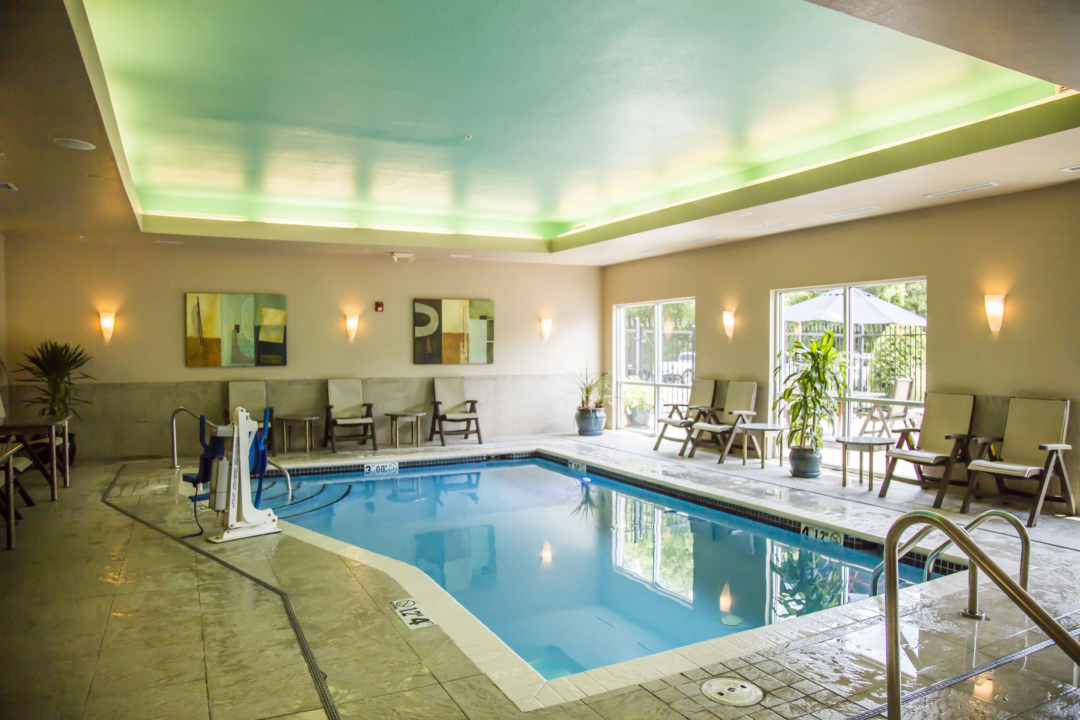 Una piscina interior con superficie de agua cristalina, rodeada de sillones de descanso y una planta en maceta.