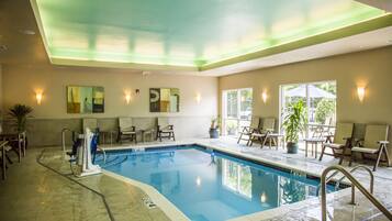 Una piscina interior con superficie de agua cristalina, rodeada de sillones de descanso y una planta en maceta.