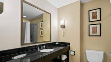 A hotel bathroom with a black vanity, two sinks, a toilet, a shower, and framed artwork on the wall.