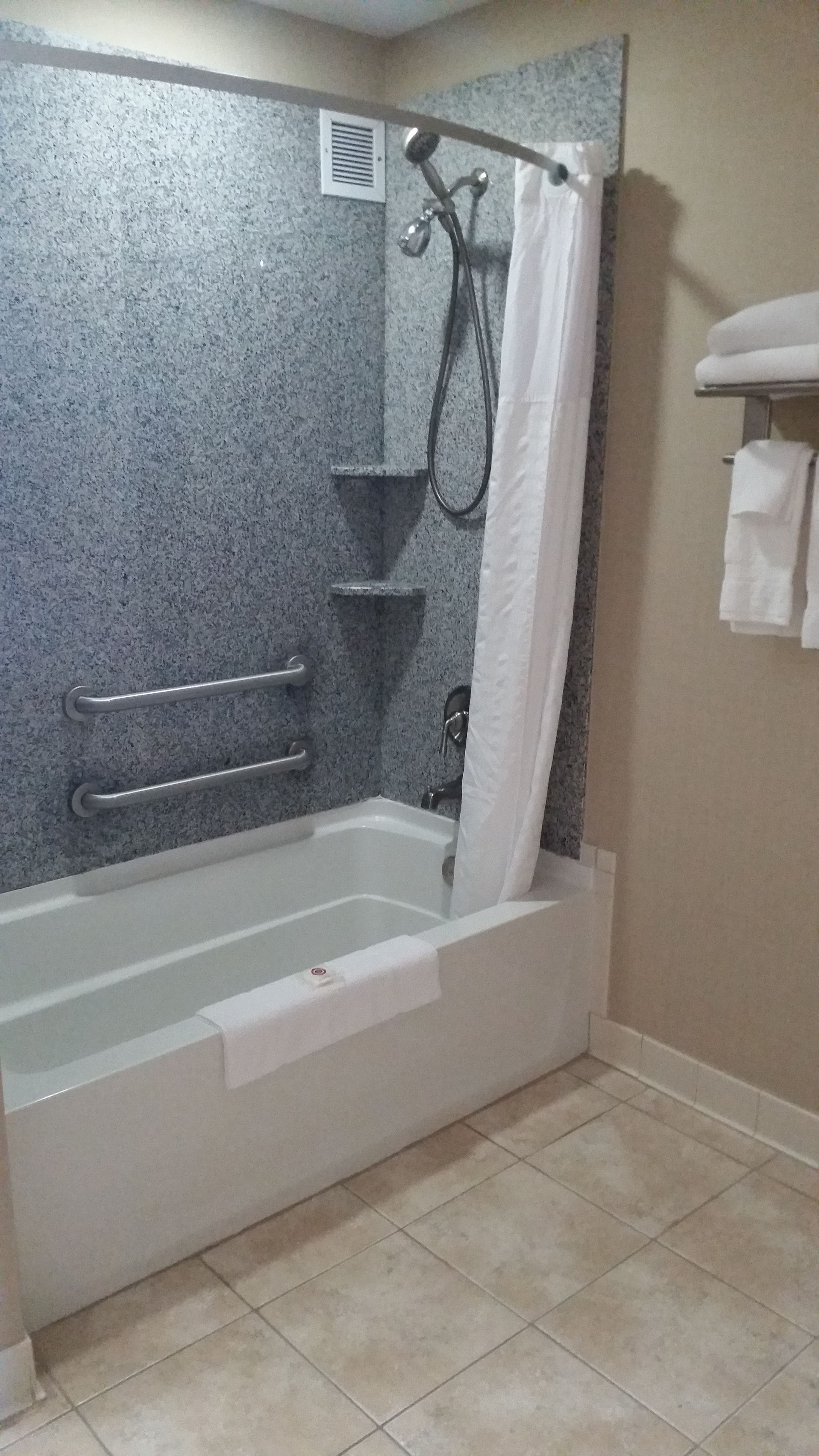 Un baño con bañera, barras de apoyo, cabezal de ducha y un perchero para toallas.