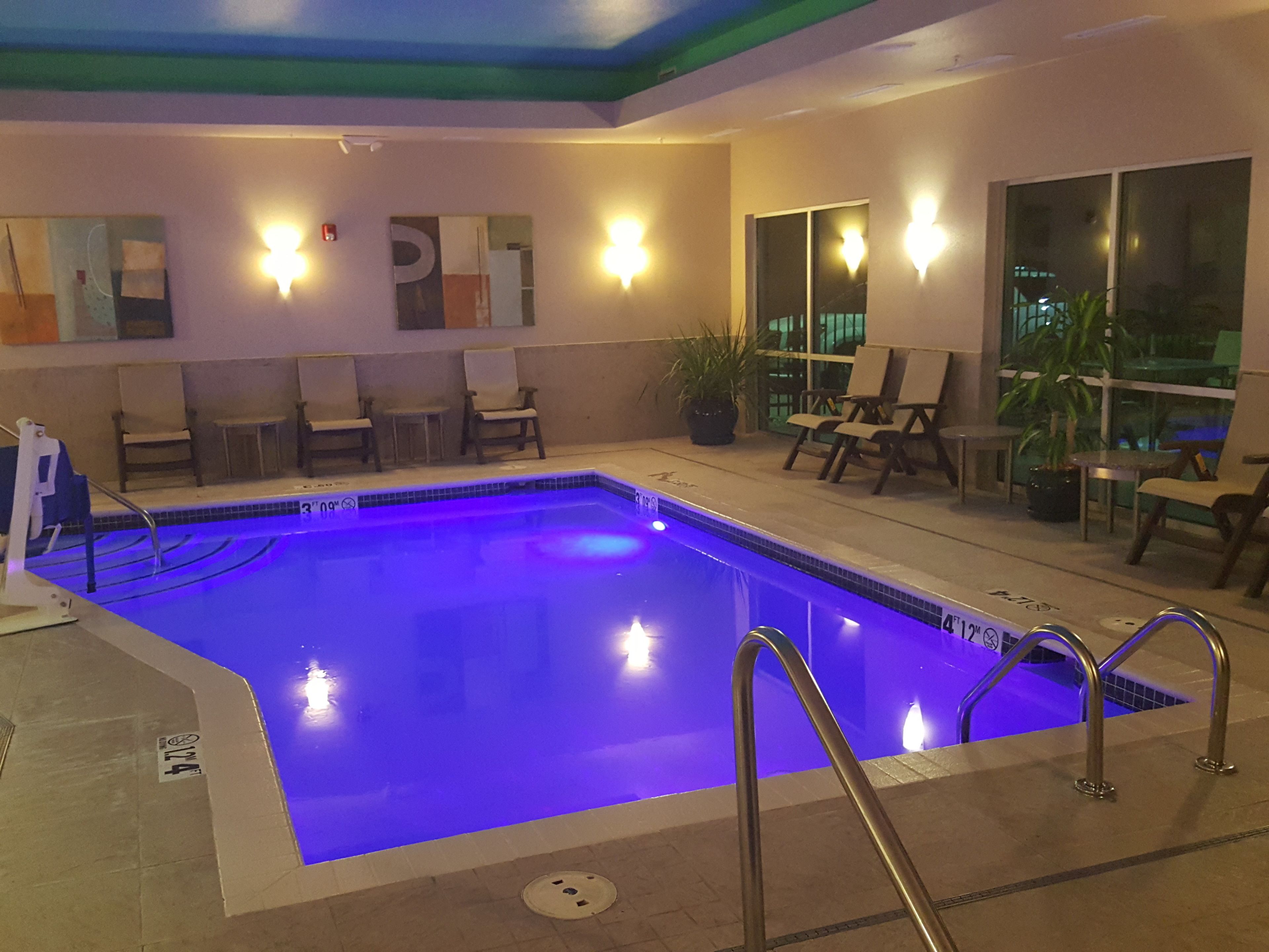 Une piscine intérieure éclairée de lumières bleues, entourée de chaises longues et agrémentée d’une plante en pot.