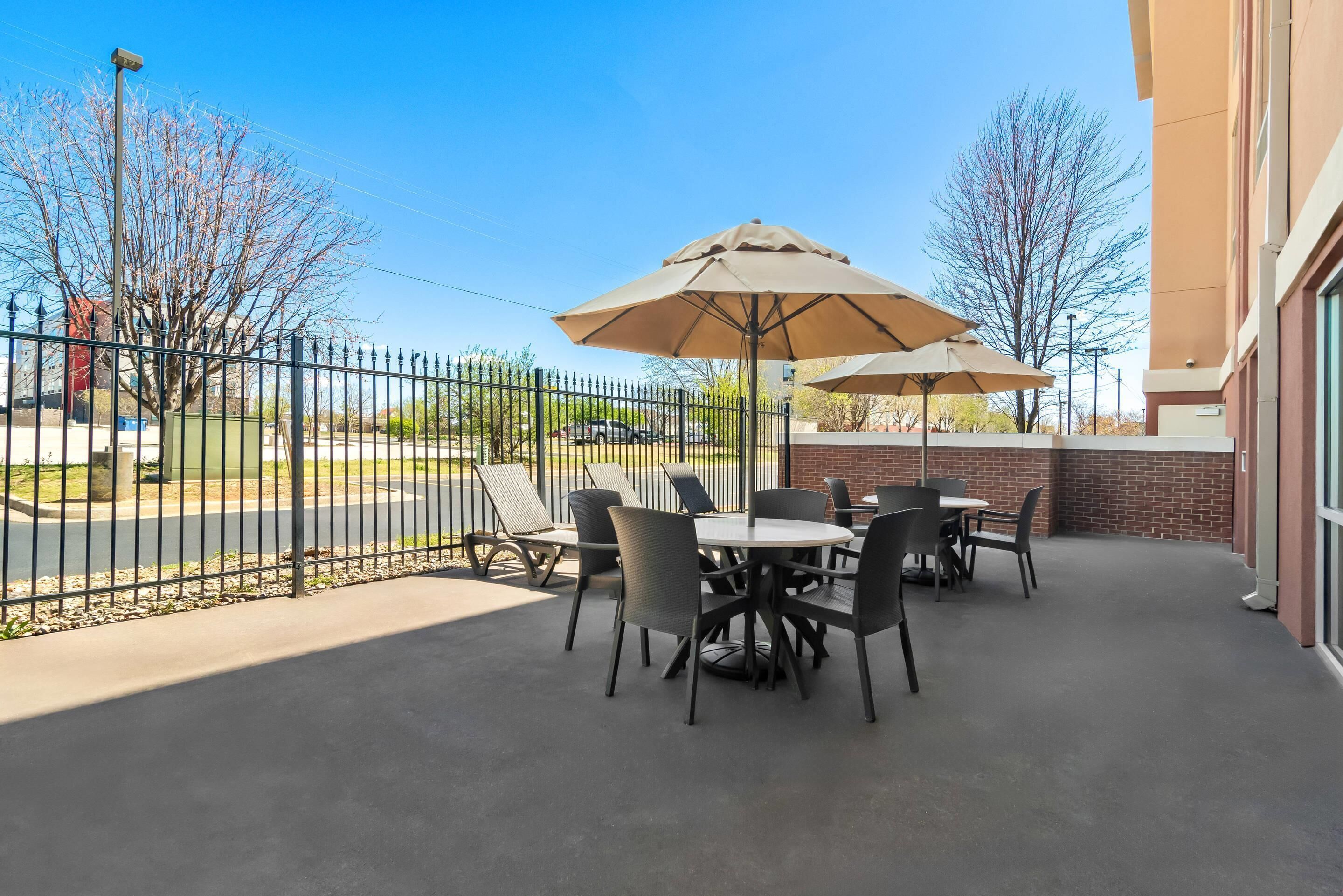 An outdoor patio with tables and chairs, umbrellas, and a brick wall.