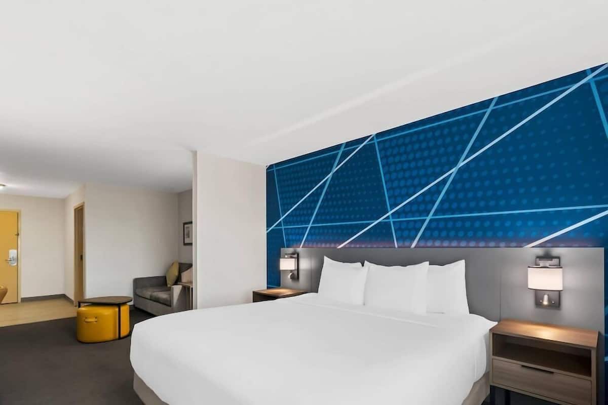 Habitación de hotel con una cama grande, un sofá, una mesita y una pared con diseños geométricos.
