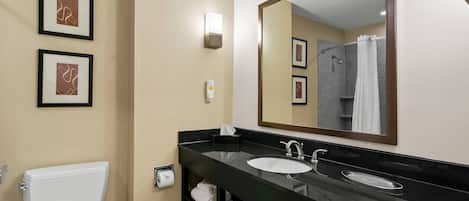 Un baño moderno con un lavamanos negro, inodoro blanco y un espejo grande. Hay cuadros enmarcados en la pared y un perchero debajo del lavamanos.