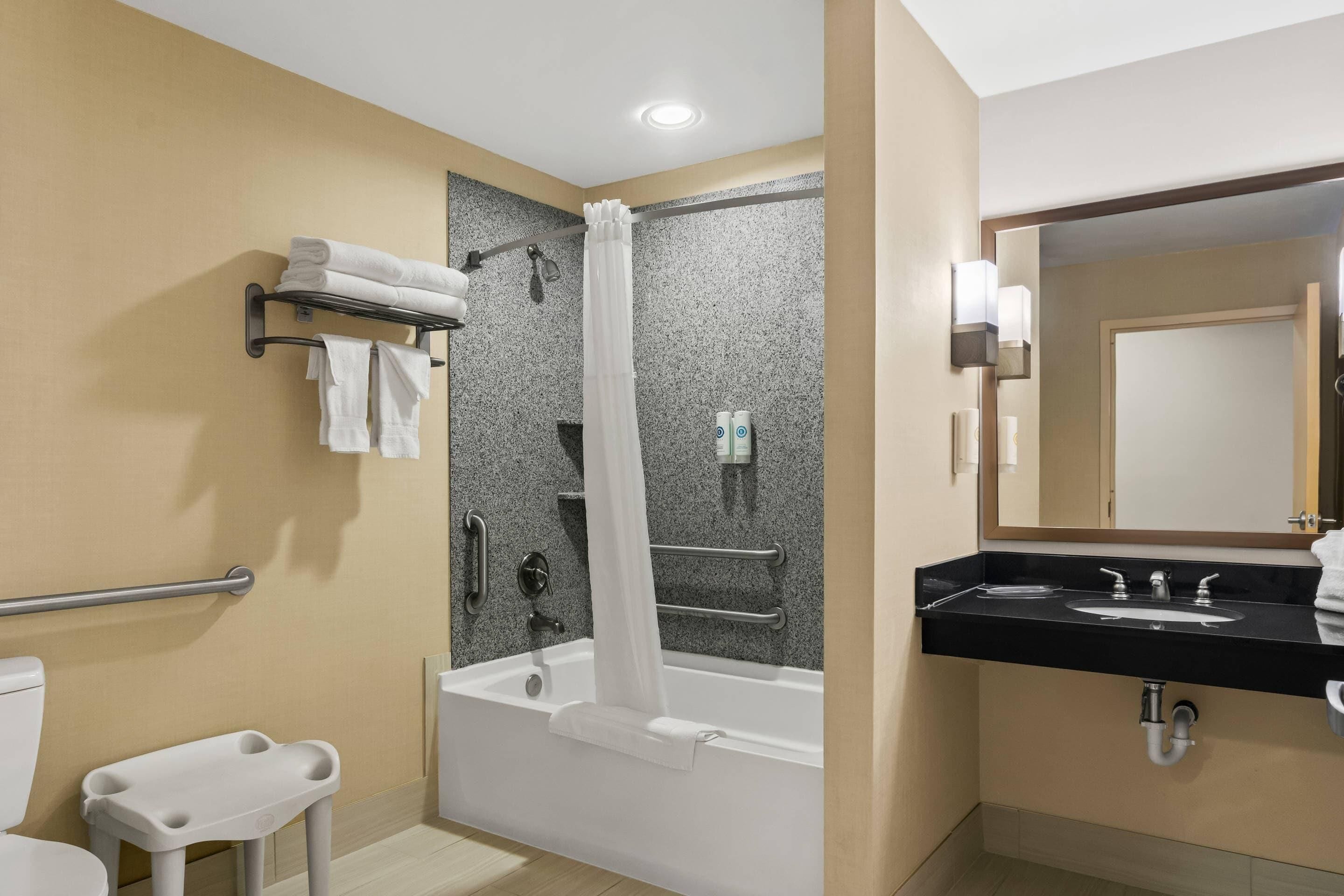 A modern bathroom with a bathtub, a shower with a curtain, a vanity with a sink, and a toilet.