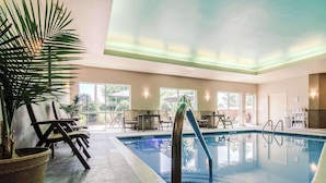 An indoor swimming pool with a clear view of the pool area, including the poolside seating and surrounding plants.