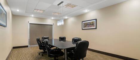 A conference room with a rectangular table, black leather chairs, recessed ceiling lights, patterned carpet, and framed artwork on the walls.