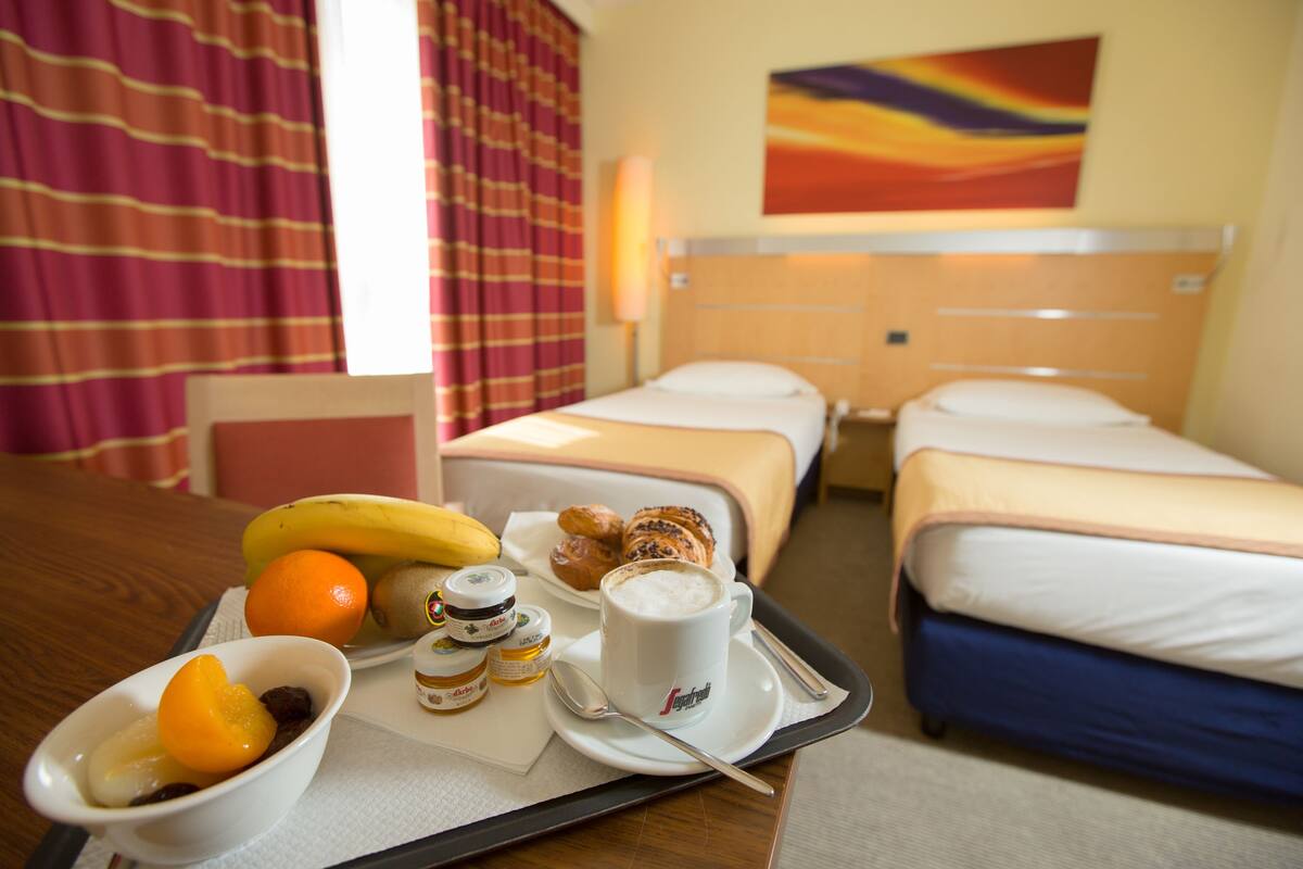 A hotel room with two beds, a dining table with breakfast items, and a colorful wall mural.