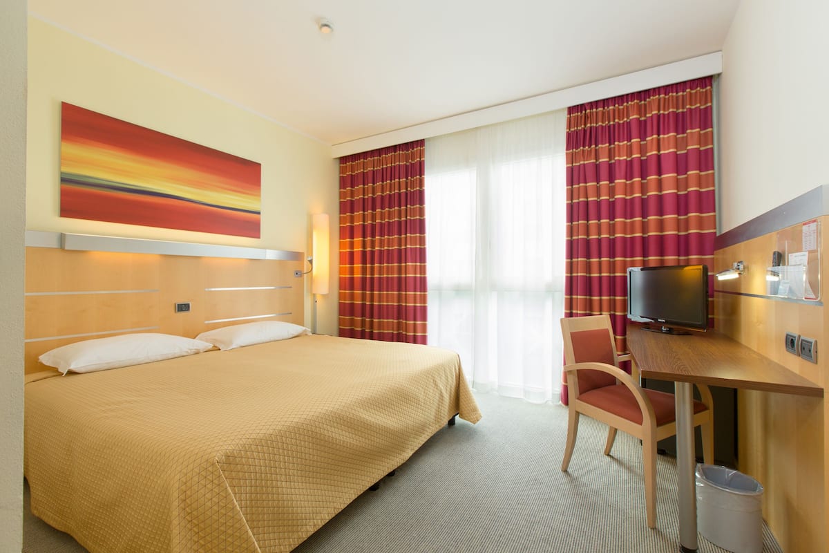 A hotel room with a bed, a desk, a television, and curtains.
