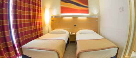 A hotel room with two beds, a large window, and a painting above the beds.