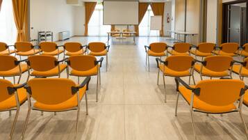 Un salón de conferencias con filas de sillas naranjas, una pantalla grande y una pizarra.