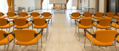 Un salón de conferencias con filas de sillas naranjas, una pantalla grande y una pizarra.