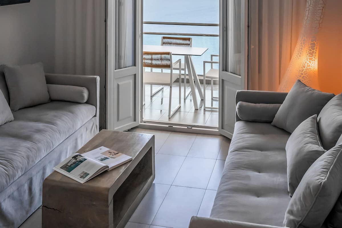 A modern hotel room with a balcony, a sofa, a coffee table, and a view of the sea.