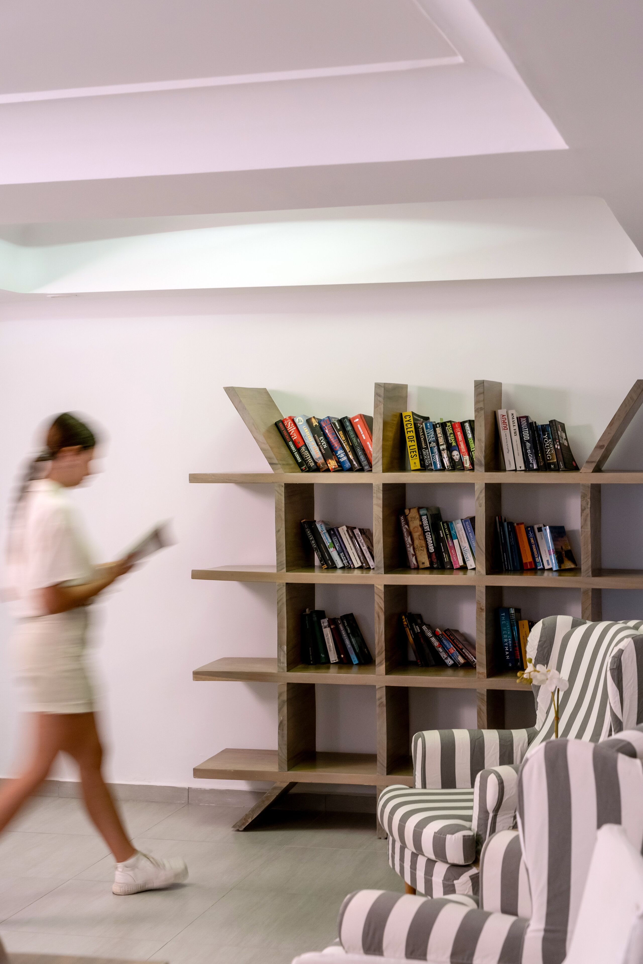 Un interior moderno con una estantería, sillones a rayas y una persona caminando.