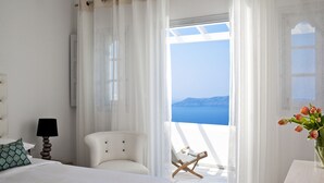 A hotel room with a bed, a chair, a lamp, and a view of the sea. - Belvedere Suites (Santorini)