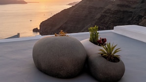 A rooftop terrace with large stone planters and a view of the sea at sunset. - Belvedere Suites (Santorini)