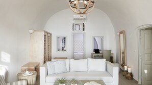 A spacious living room with a white sofa, a coffee table with plants, and a chandelier. - Belvedere Suites (Santorini)