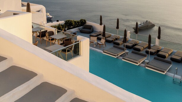 A poolside area with lounge chairs and umbrellas, overlooking a body of water with a distant coastline. - Belvedere Suites (Santorini)