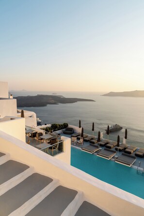 Un espace aménagé au bord de la piscine, avec des chaises longues et des parasols, offrant une vue sur une étendue d’eau et une côte lointaine.
