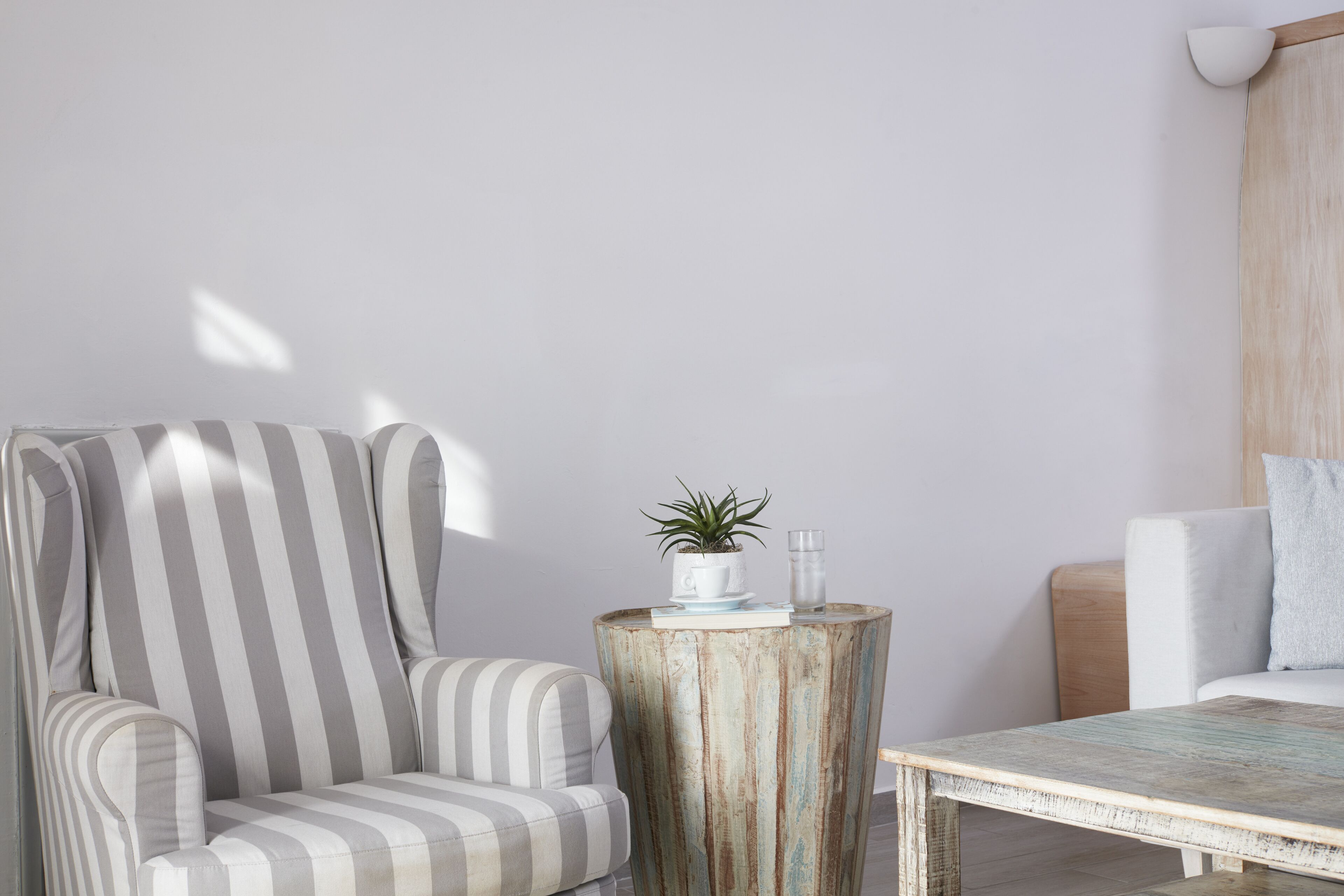 A striped armchair, a rustic wooden side table with a plant and glass, and a white sofa in a bright room with a wooden accent wall.