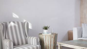A striped armchair, a rustic wooden side table with a plant and glass, and a white sofa in a bright room with a wooden accent wall.