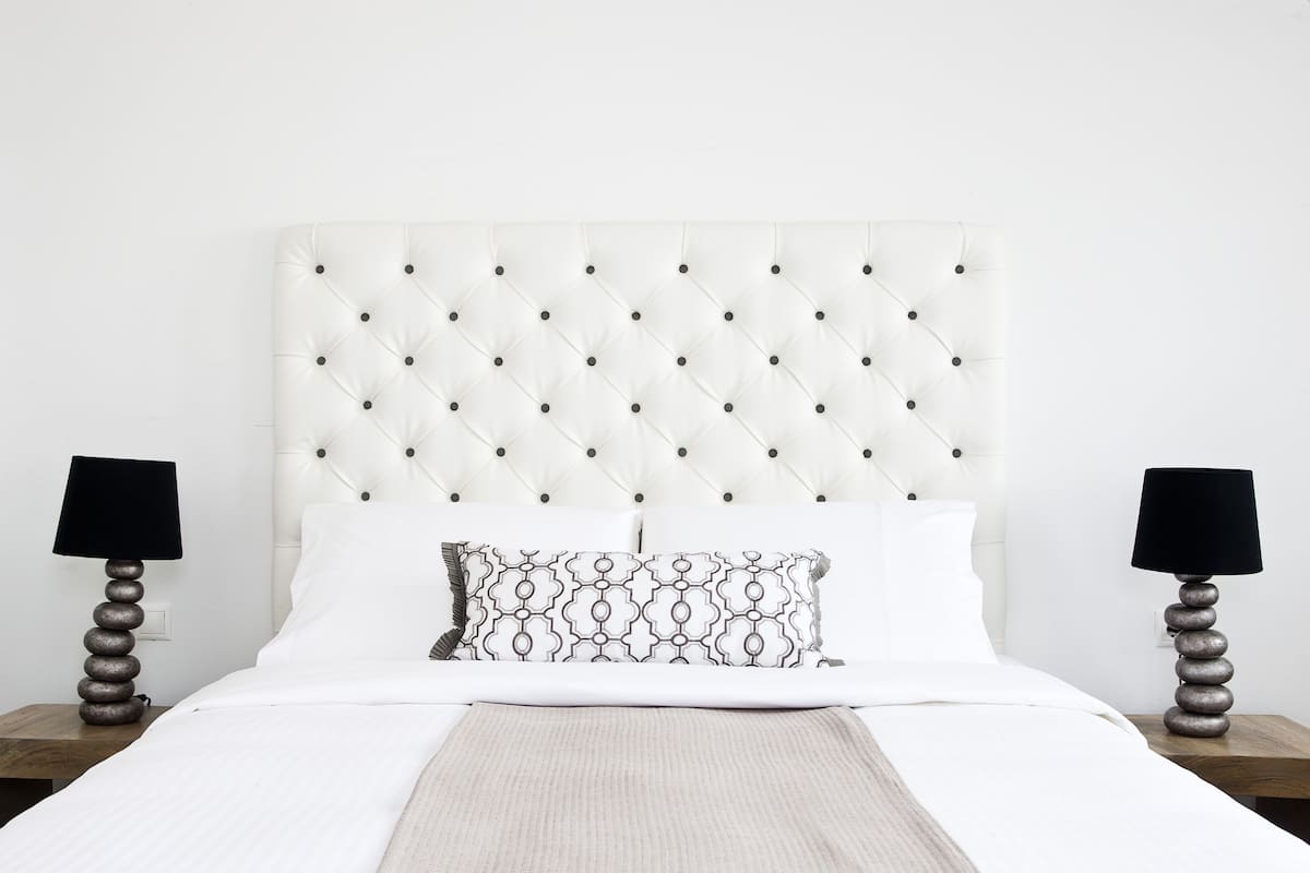 A neatly made bed with a tufted headboard, two bedside tables with lamps, and a patterned throw pillow.