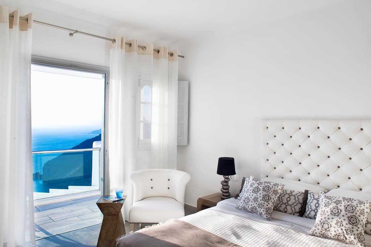 A bedroom with a large bed, a chair, a nightstand, and a view of the ocean.