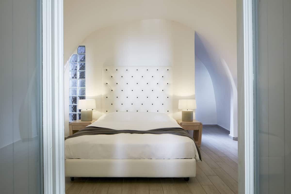 A modern bedroom with a large bed, two bedside tables, and a unique wall-mounted headboard.
